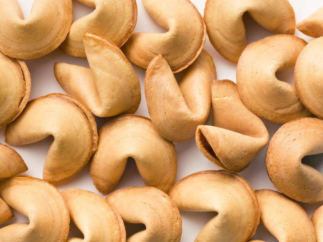 A collection of golden fortune cookies arranged closely together on a white background.