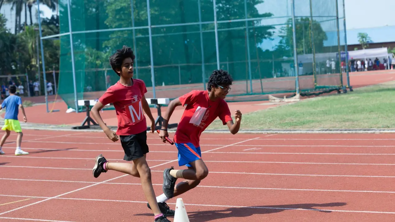 Two boys running a relay race as one hands off the baton to the other on a track.