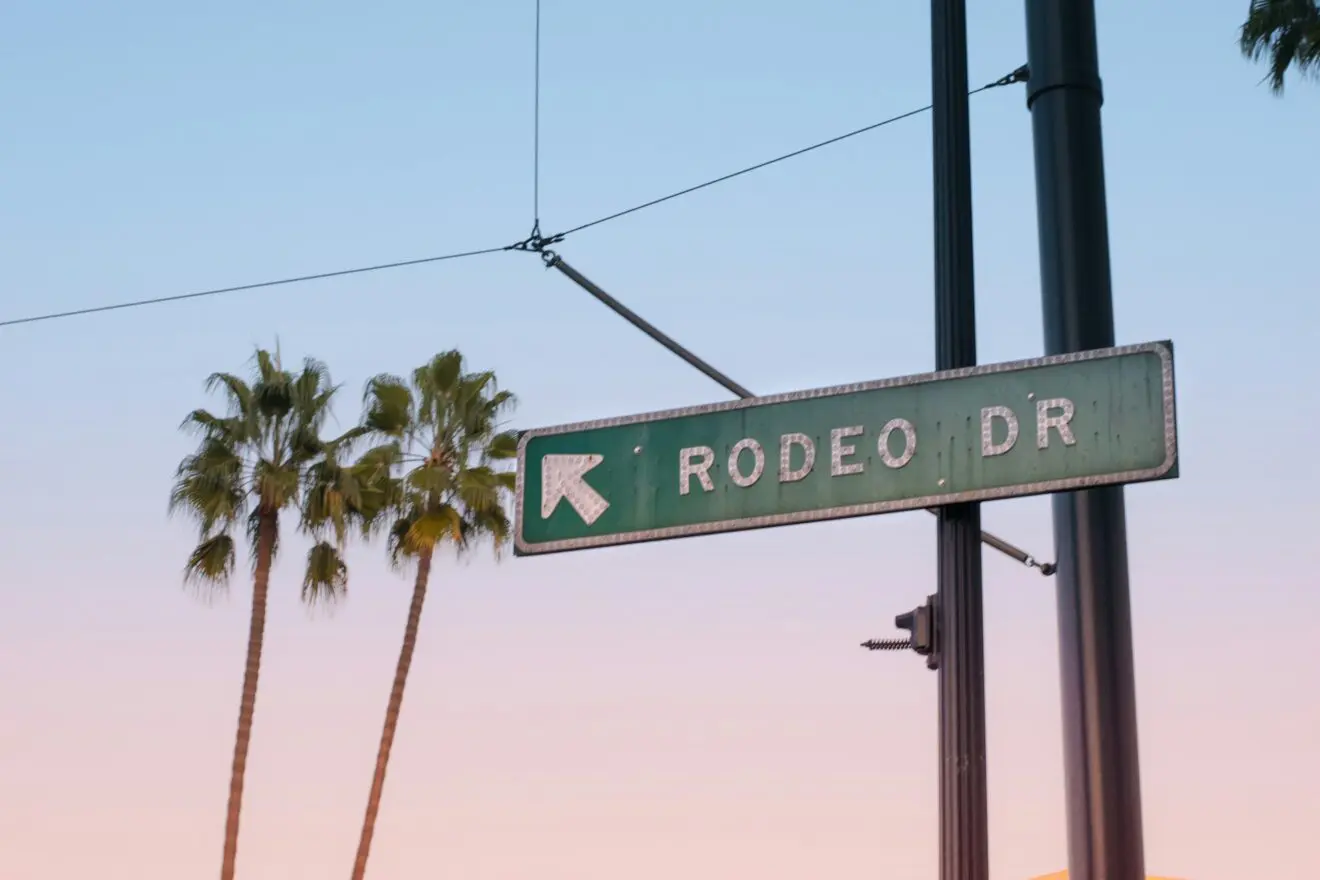 Street sign for Rodeo Drive in Beverly Hills with palm trees in the background at sunset.